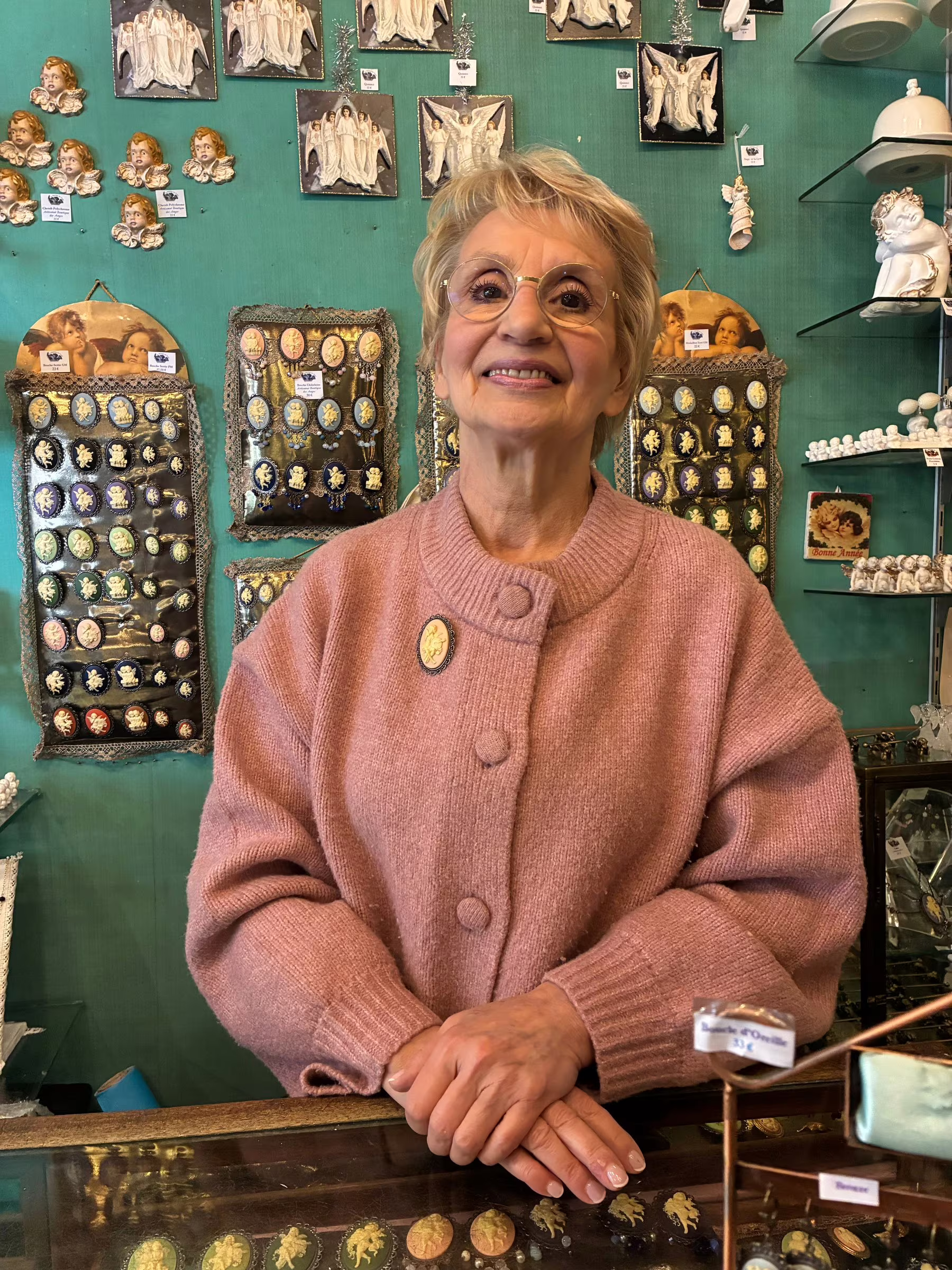 Brigitte de Cuyper derrière le comptoir du Magasin, devant le mur de camées.